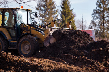 The excavator backfills the pit with the front bucket and moves soil around the construction site. Close-up. Heavy construction equipment