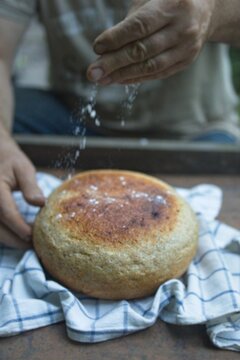 Baker's hand sprinkles flour on fresh bread close-up. A man finishes baking, decorates warm bread. Traditional village recipe, home baking concept