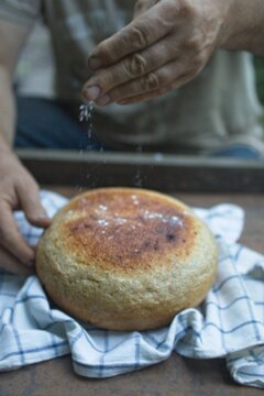 Baker's hand sprinkles flour on fresh bread close-up. A man finishes baking, decorates warm bread. Traditional village recipe, home baking concept