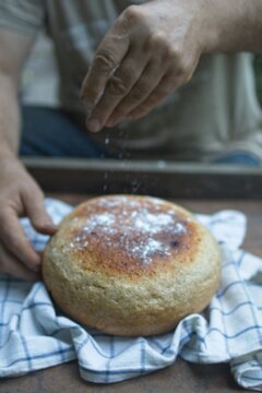 Baker's hand sprinkles flour on fresh bread close-up. A man finishes baking, decorates warm bread. Traditional village recipe, home baking concept