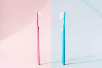 Pink toothbrush against pink background and blue toothbrush against blue background.