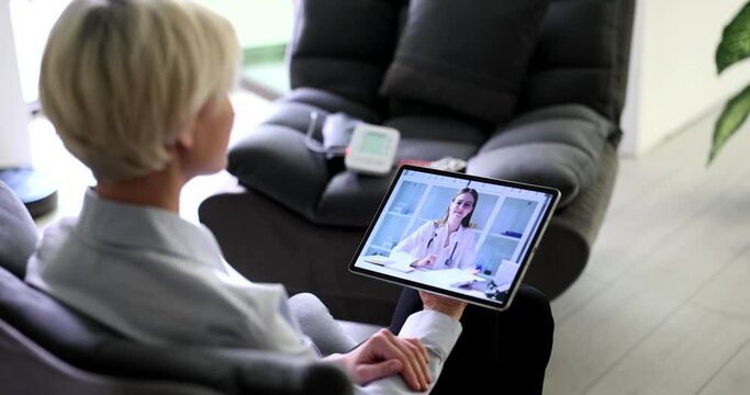 Blonde woman talks on video call with doctor via tablet complaining on pain in heart. Female patient at online consultation with specialist slow motion