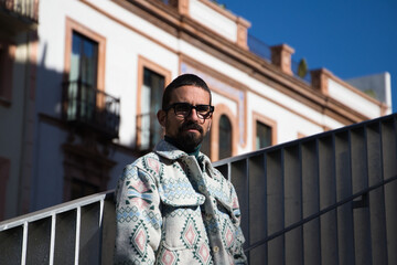 Portrait of young handsome gay man with beard and glasses. The man is dressed casually and in modern clothes and is serious and angry.