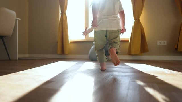 Happy family. Baby feet walk on floor towards mother. Child makes steps barefoot on parquet floor in children room. Son runs to his mother on the laminate with his bare feet. happy baby first steps