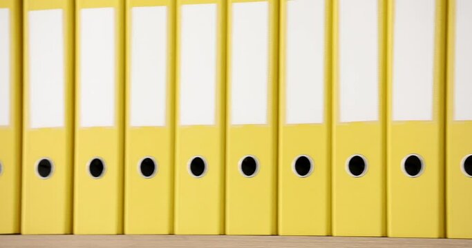 Organized structure of yellow ring binders put on rack shelves in row in office. Big folders with archive materials and accounting documents for work