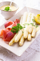 Traditional German white asparagus with air dried Parma ham and tomatoes served as close-up on a design plate