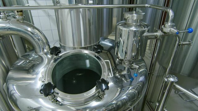 Arc shot of large stainless steel whirlpool vat for purifying beer wort at independent craft brewery, with pipes and sight glass on top