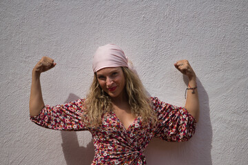 Middle-aged blonde woman, wearing a flower dress and a pink scarf of the fight against cancer, with...