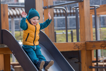 A little boy walks on the playground in the spring. The child is having fun riding down the hill. Childhood and child development.