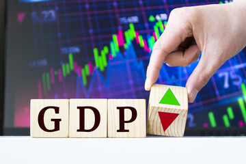 A hand rotates a wooden cube to indicate the fall or rise of GDP