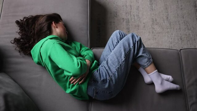Young woman have stomach  pain lying on couch, top view