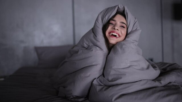 Young happy woman under duvet in her bed