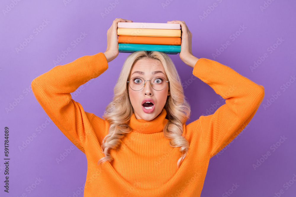 Poster Photo of impressed pretty girl stylish hairdo dressed orange sweater hold book on head open mouth isolated on purple color background