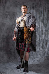 A brutal medieval Scottish warrior in a kilt with a sword in his hands