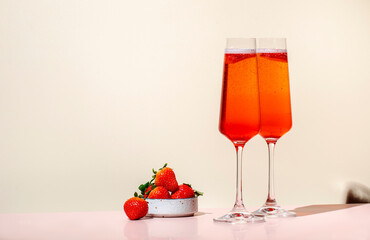 Rossini summer alcoholic cocktail drink with sparkling wine or prosecco, strawberry puree and ice in champagne glasses. Beige pink vanilla background, hard light, shadow pattern