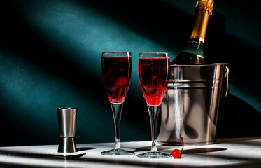 Kir Royale cocktail with black currant liqueur, prosecco wine and red cocktail cherry. Dark green background, hard light and shadow pattern