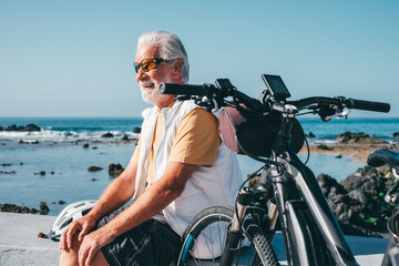 Happy active bearded senior man with bike bicycle sits at the beach. Authentic retirement life and healthy lifestyle concept. Horizon over the sea