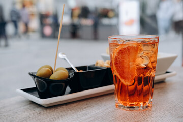 Traditional Italian aperitif cocktail aperol spritz with ice and olives and snaks in Italian bar,...