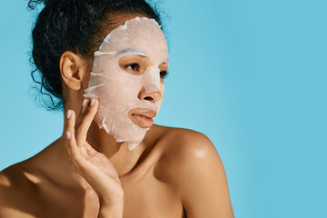 Facial hydrating and rejuvenation procedure. African American woman with moisturizing skincare mask on blue background, high quality