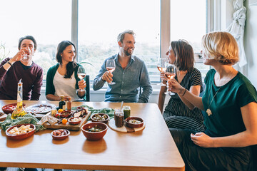 group of friends sitting around a table full of appetizers such as dips, breadsticks, olives, and other snacks typically served during an aperitif. People are talking and smiling, each with a glass