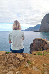 The girl sits on the edge of a cliff and enjoys nature.
