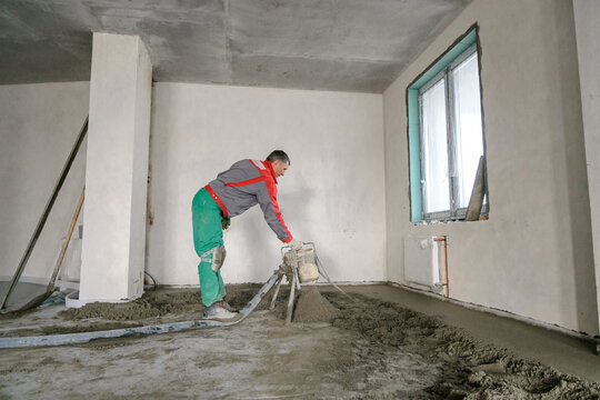 A builder in work clothes is doing his job, leveling the floor, pouring mortar