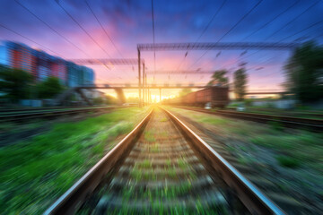 Fototapeta na wymiar Railroad with motion blur effect at sunset in summer. Industrial landscape with railway station and blurred background with colorful sky, green grass. Railway platform in speed motion. Concept