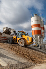 The front loader unloads the crushed stone into the making machine concrete. Against the background...