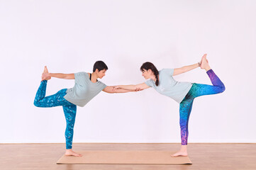 Fototapeta premium Two girls doing standing yoga, facing each other, holding one foot with one hand and holding hands with the other hand