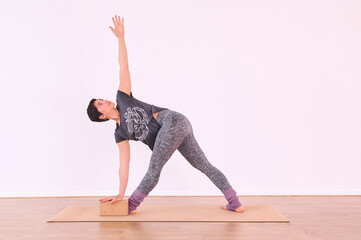 Naklejka premium A young woman performing the Warrior pose, Virabhadrasana, using a cork yoga block for support.