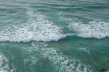 Fototapeta na wymiar Ocean foamy waves approaching rocky shore. Top view.