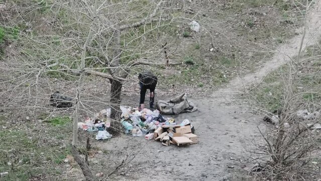 A homeless man rummages through the garbage sorting plastic bottles. Homeless sort trash looking for bottles, metal, cardboard, and valuables. Poverty. Homeless looking for food and useful items.