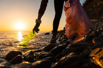 Earth day. A volunteer take a plastic bottle by the sea or river holding a plastic trash bag....