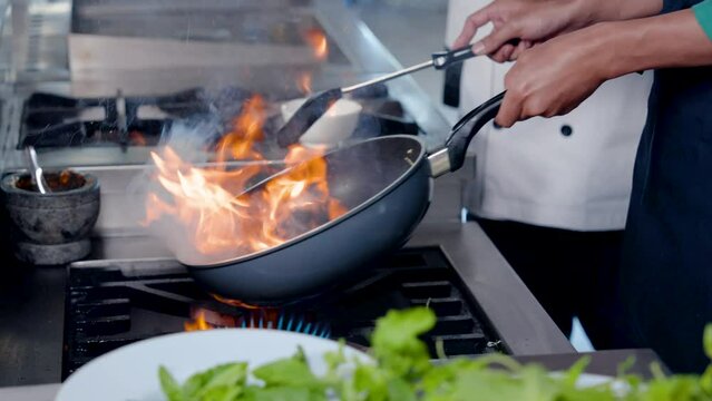 4K Slow, Close-up pan with chef's hand holding pan handle firmly, chef lifts pan stirs by hand, technique for skilled chefs, stir fried red cabbage exciting fire, gas stove with hot fire for cooking.