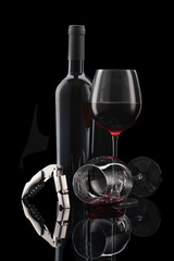 Glass of red wine with bottle and wine cutlery in front of black background