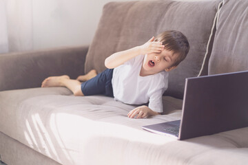 The boy is tired and yawns near on
 laptop