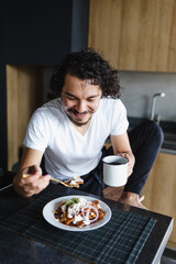 latin man eating chilaquiles mexican breakfast at home apartment in Mexico Latin America, hispanic...
