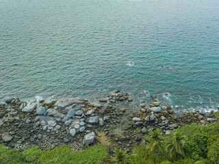 .aerial top view the rock beach full of stones in several size along around the island. .smooth waves hit on the rocks beside the green sea..green water background.