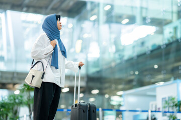 An Asian Muslim wearing a blue hijab is preparing for a vacation and she is at the airport. She is waiting for her friends, Muslim travelers.