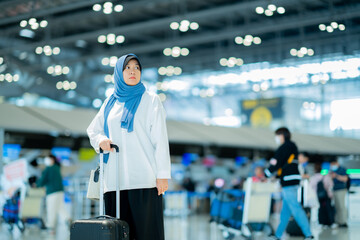 An Asian Muslim wearing a blue hijab is preparing for a vacation and she is at the airport. She is waiting for her friends, Muslim travelers.
