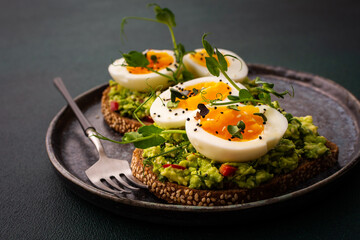 Sandwiches with rye bread and guacamole, with boiled eggs and microgreens of peas and radishes and sesame seeds, a plate with sandwiches close-up on a green background