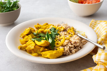 Healthy lunches, brown rice with chicken with turmeric and curry seasoning, fresh vegetables and herbs, water with lemon