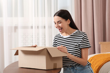 Emotional young woman opening parcel at home. Internet shopping