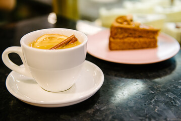 Fruit tea with cinnamon in a white cup on a white plate. Against the background of dessert on a pink plate
