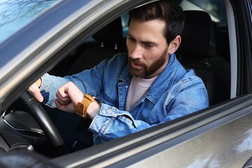 Emotional man checking time on watch in car. Being late concept - obrazy, fototapety, plakaty