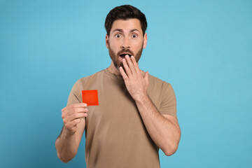 Emotional man holding condom on light blue background. Safe sex