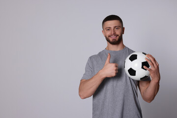 Athletic young man with soccer ball showing thumb up on light grey background. Space for text