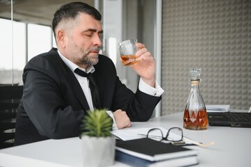 Old business man is drinking alchool at the office
