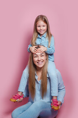 Beautiful young blonde mother sitting on floor with her cute little child and smiling to camera on pink background