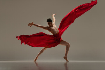 Classic and modern ballet combination. Handsome young male dancer performing with red fabric...